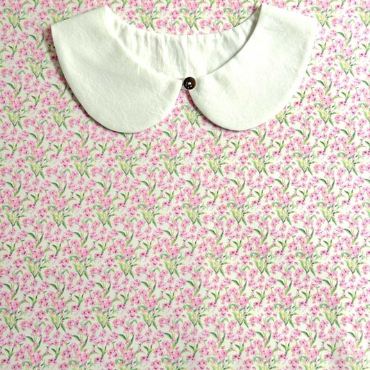 A white collar with a button is displayed against a background of a floral print fabric.