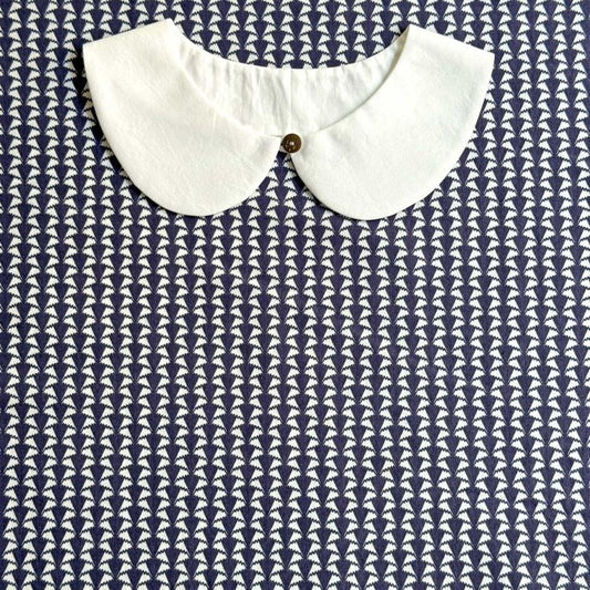 A white collar is displayed against a blue and white patterned fabric background.