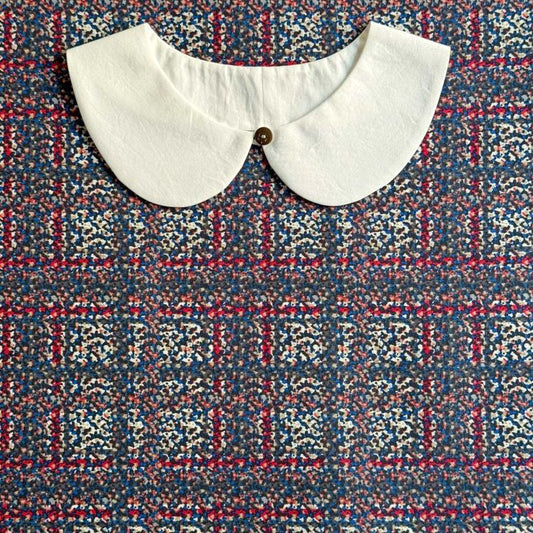 A white collar is displayed on a colorful patterned fabric.