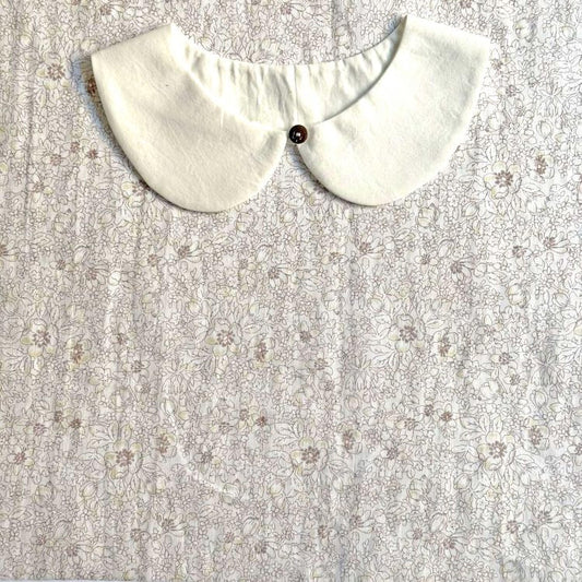 A white collar with a button is displayed on a fabric with a floral pattern.