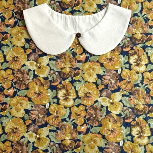 a white collar with a button, set against a background of a colorful floral print.