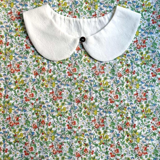 a white collar with a button, set against a background of a colorful floral print.