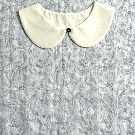 A white collar is displayed on a gray floral fabric background.