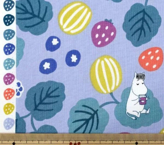 a fabric with a playful pattern of fruits and leaves, including strawberries, blueberries, and a small white character. The fabric is displayed on a wooden ruler, which is placed on a wooden surface.