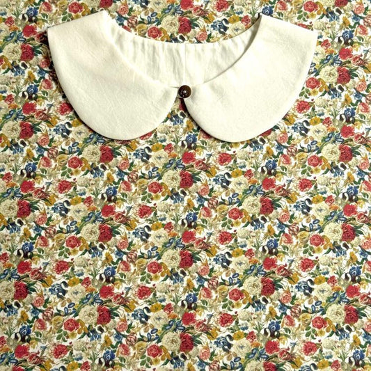 A white collar with a button is displayed against a colorful floral print background.
