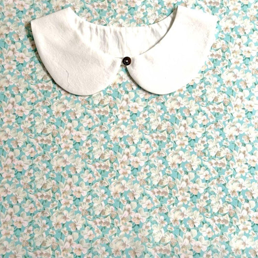 A white collar with a button is displayed against a background of a floral print fabric.