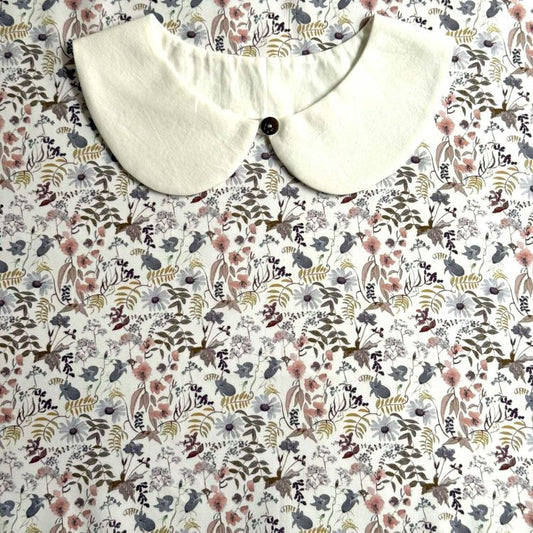 a white collar with a button, placed on a floral print fabric.