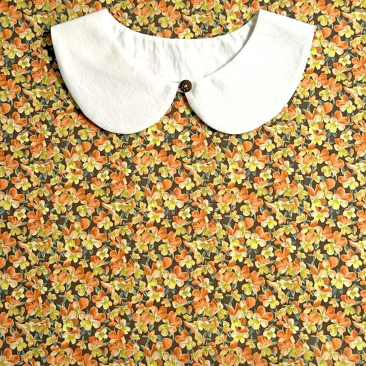 a white collar with a button, set against a background of a floral print with orange and yellow flowers.
