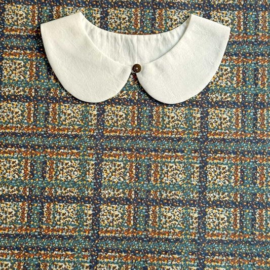 a white collar with a button, placed on a colorful fabric with a geometric pattern.