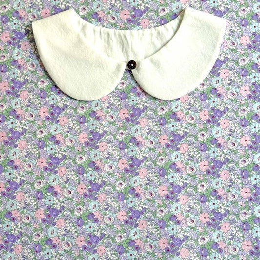 a white collar with a button, set against a background of a floral print in shades of purple and pink.
