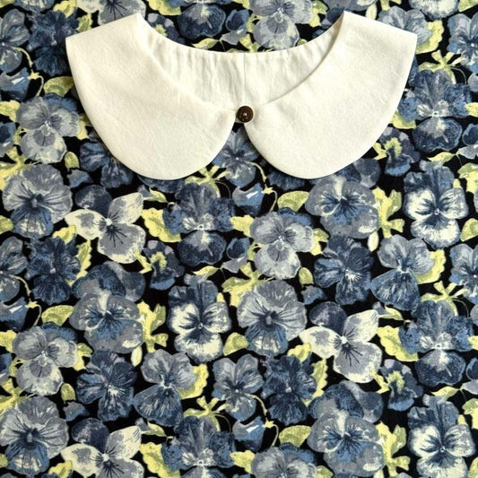 a white collar with a button, set against a background of a floral print with blue and yellow flowers.