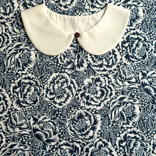 a white collar with a button, set against a background with a black and white floral pattern.