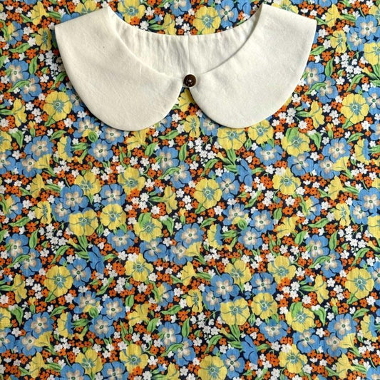 a white collar with a button, set against a background of a colorful floral print.