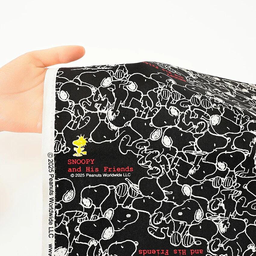 A hand holding a piece of fabric with a repeating pattern of black and white cartoon characters resembling the Peanuts characters.