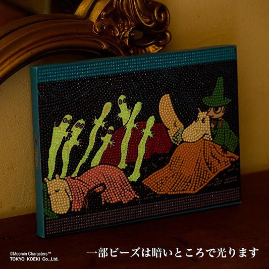 The image is a colorful painting or artwork featuring a whimsical scene with various characters and elements, including a character in a green hat and a character in a red hat. The painting is displayed on a wooden surface, and there is a gold-colored frame or decoration in the background.