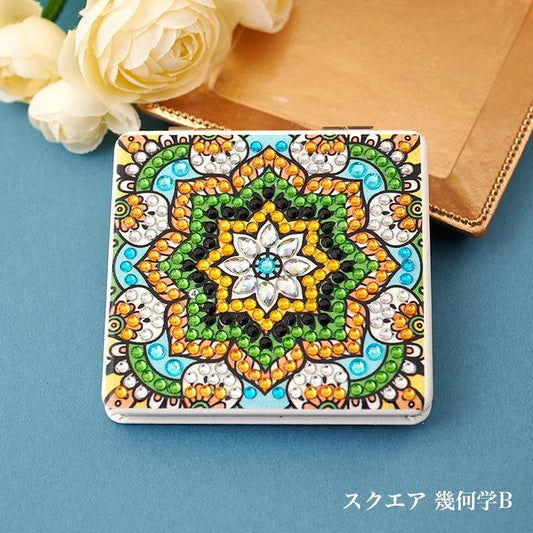 A decorative square mirror with a vibrant, colorful design featuring a central flower-like motif surrounded by intricate patterns and sparkling gemstones. The mirror is placed on a blue surface, with a bouquet of white roses visible in the background.