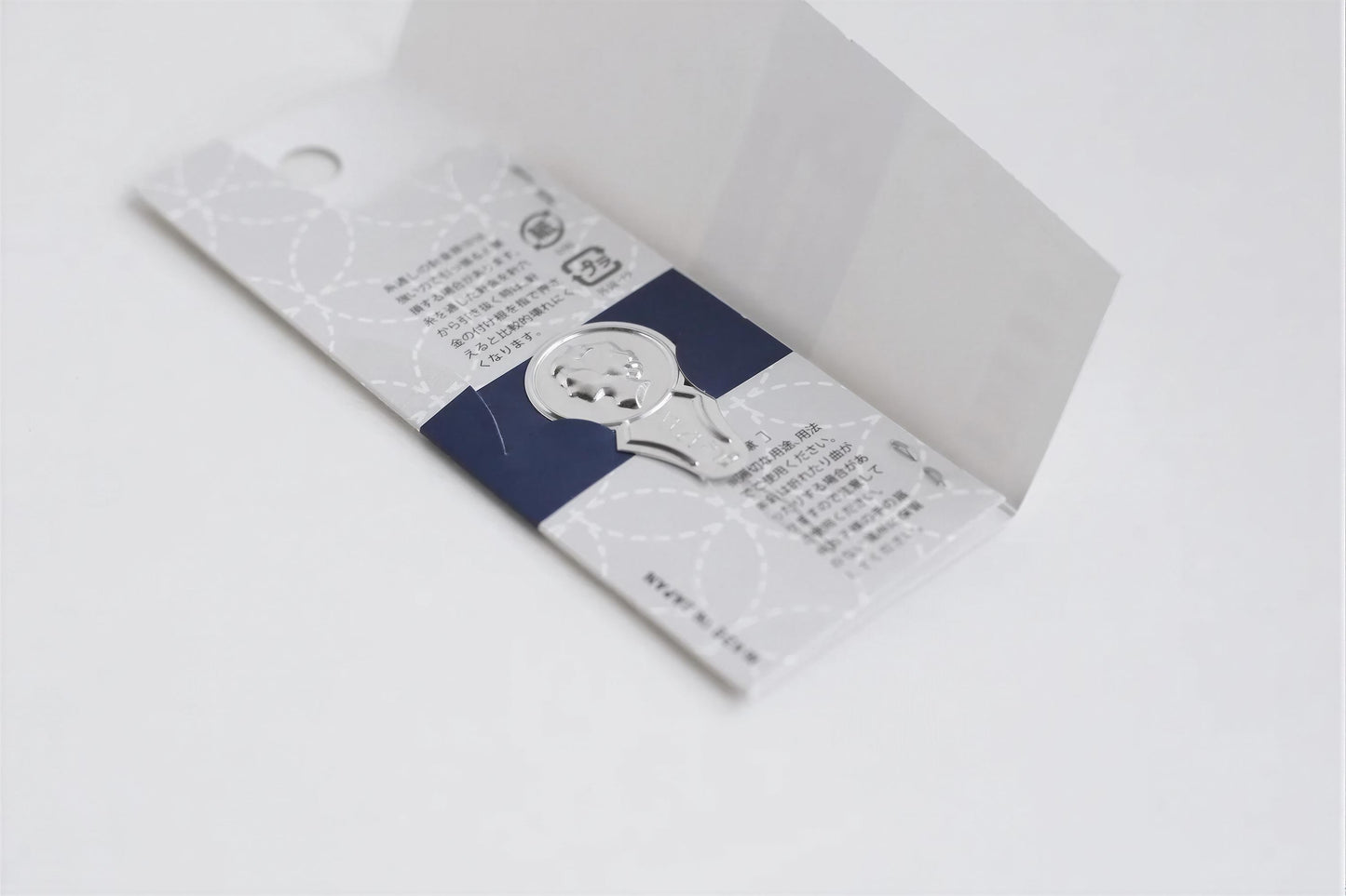 a silver paper clip with a blue and white design on it, placed on a white surface.