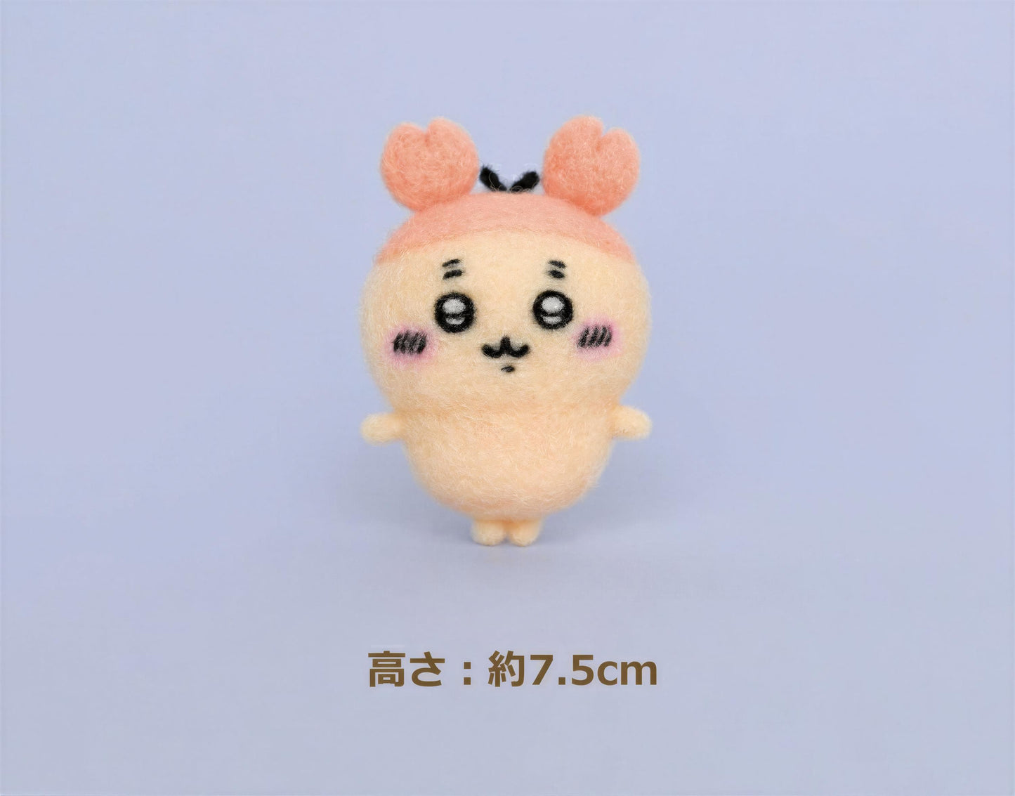 A small, cute plush toy with a pink hat and face, standing on a plain background.