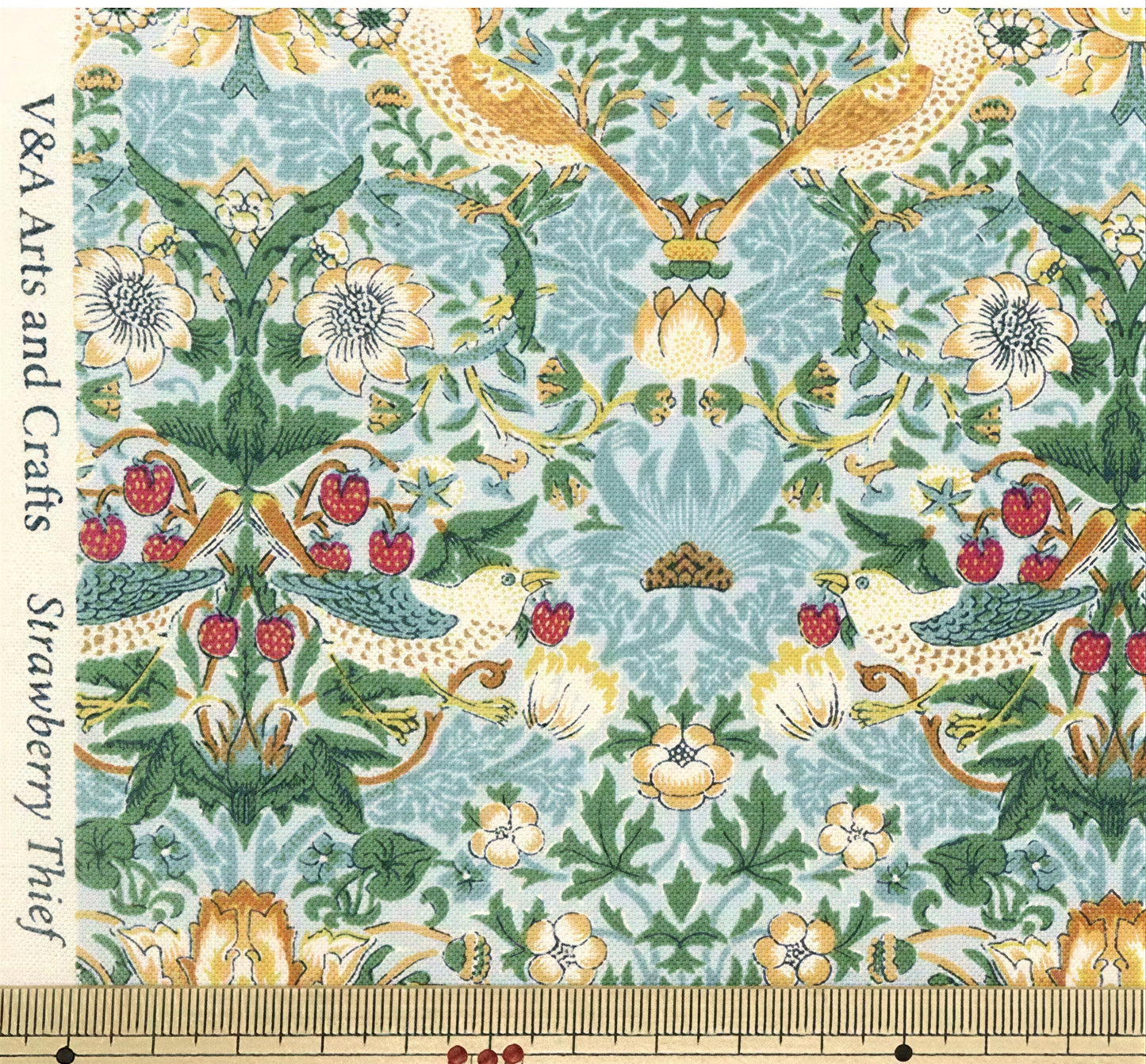 The image is a close-up of a fabric with a repeating pattern of flowers, leaves, and berries in shades of green, yellow, and red. The pattern is intricate and detailed, showcasing the craftsmanship involved in creating the fabric.