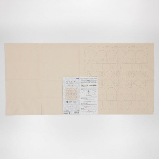 The image is a large, cream-colored fabric with a printed pattern on it. There is a small, white paper with text and diagrams next to the fabric.