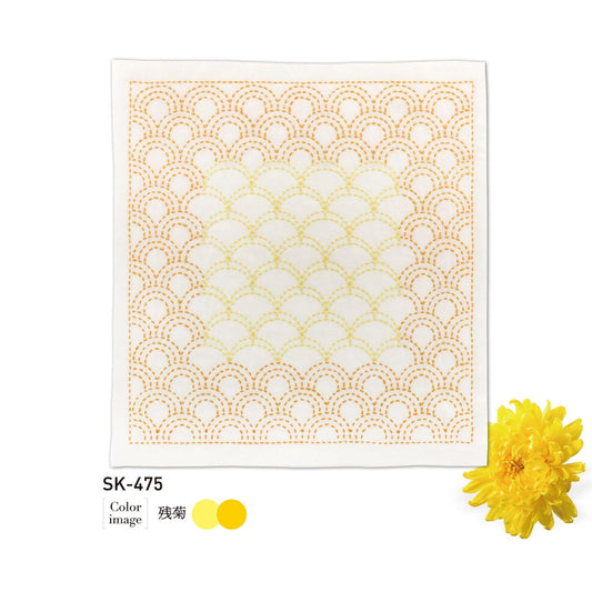 a square piece of fabric with a repeating pattern of yellow and white circles, resembling a wave or a mandala design. The fabric appears to be white, and there is a single yellow flower placed next to it.