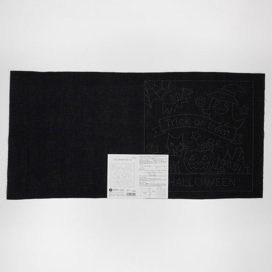 The image is a black and white photograph featuring a Halloween-themed quilt with a black background and a white label with Japanese text.