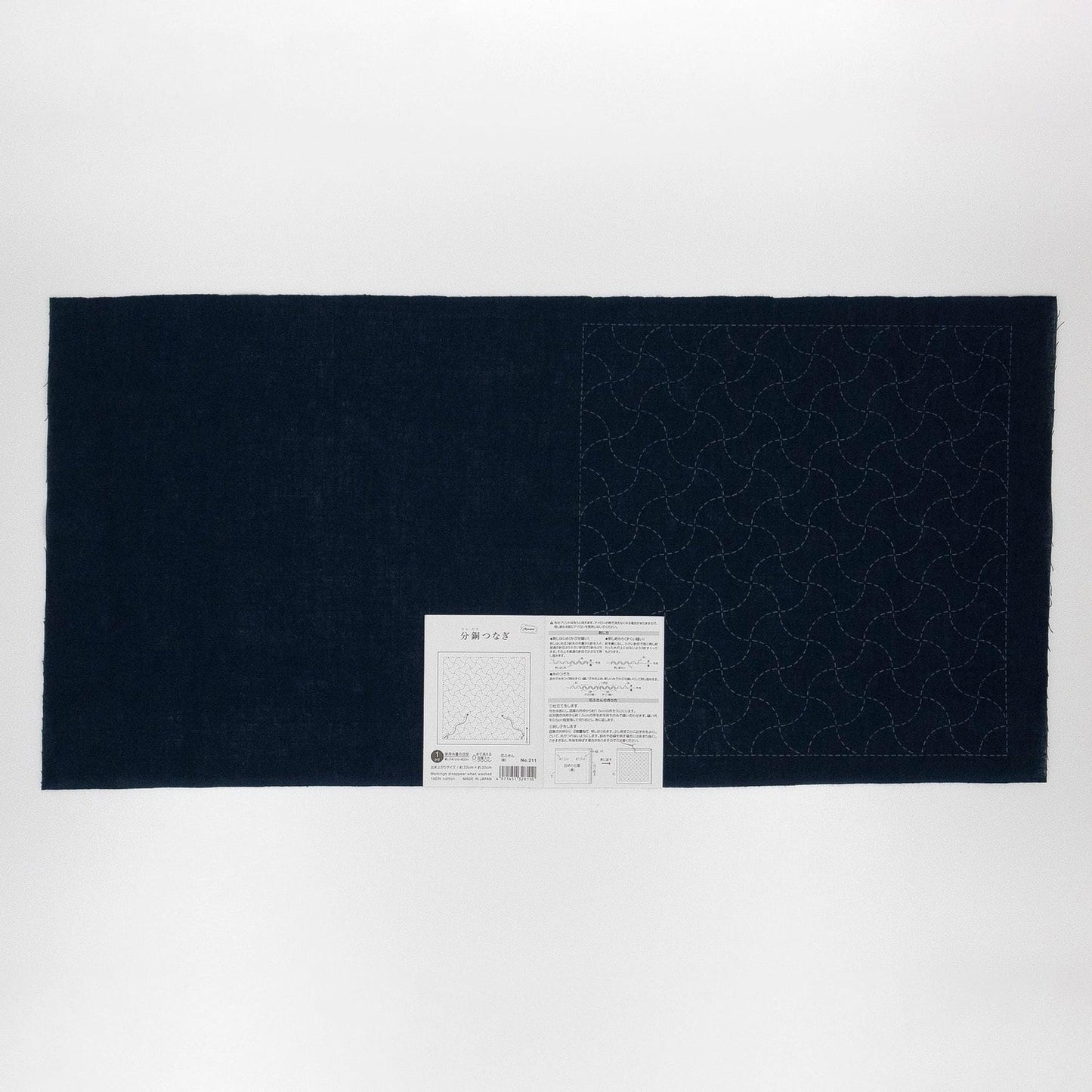 The image is a black and white photograph of a large piece of fabric with a pattern on it, accompanied by a small white label.