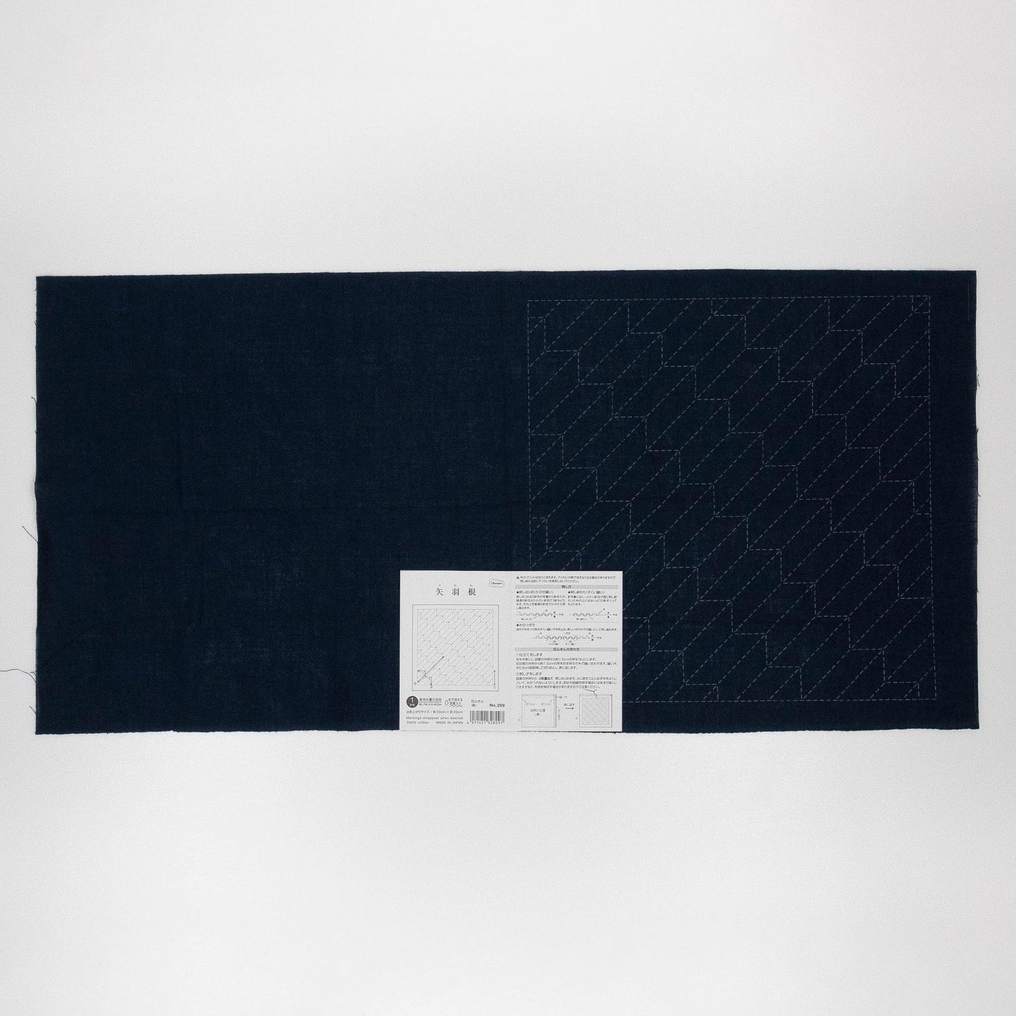 The image is a black and white photograph of a piece of fabric with a white paper attached to it, displaying a pattern or instructions.