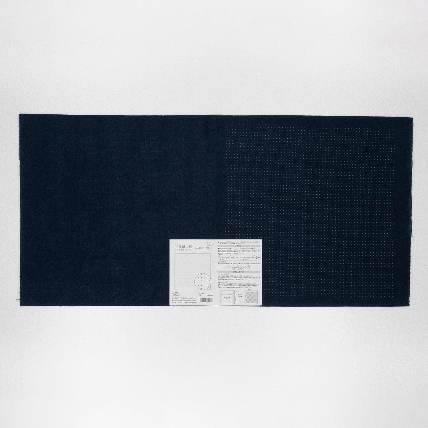 The image is a black and white photograph of a large rectangular piece of fabric or material, with a small white label or tag attached to it.