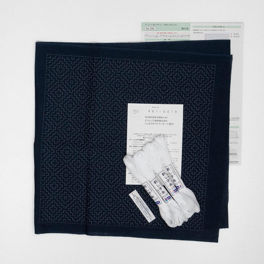 a black fabric with a geometric pattern, along with some white thread and a piece of paper with text in Japanese.