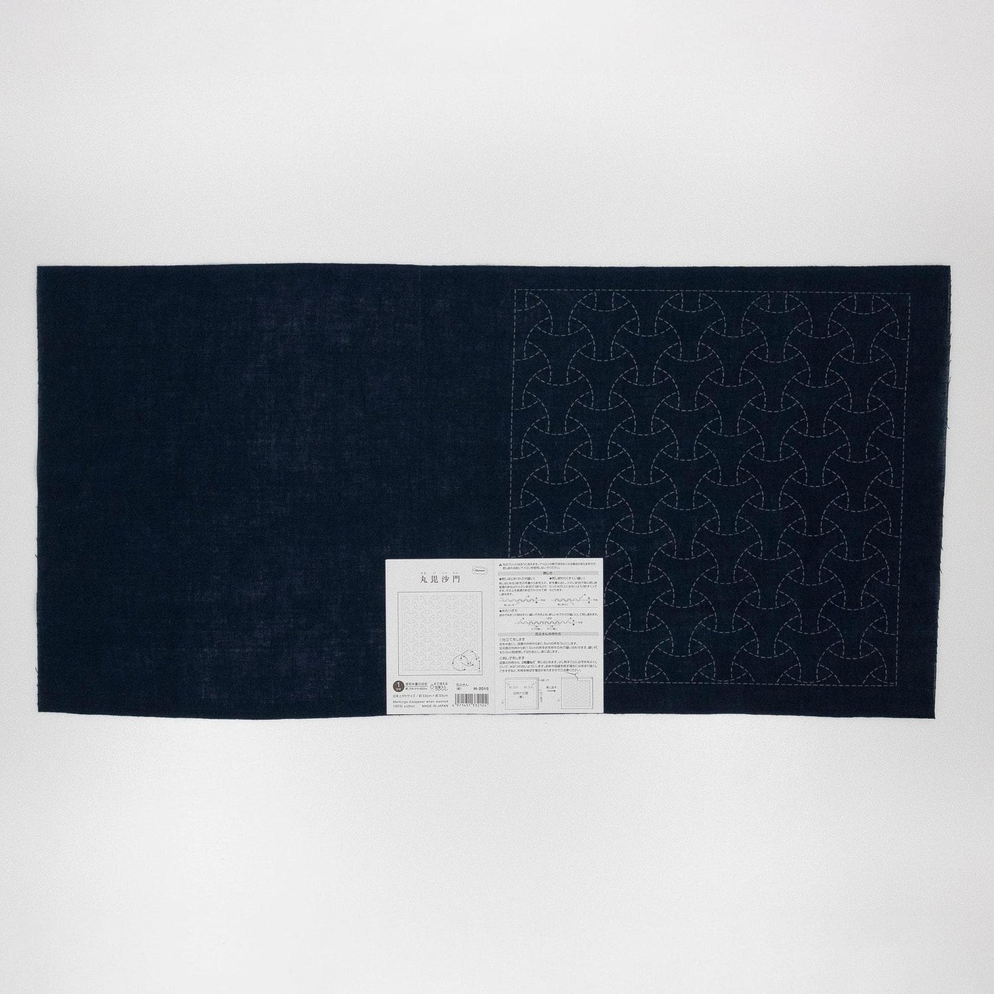 a dark fabric with a repeating pattern of circles or triangles, and there is a small white label or instruction sheet attached to the fabric.