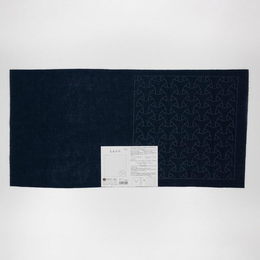 a dark fabric with a repeating pattern of circles or triangles, and there is a small white label or instruction sheet attached to the fabric.