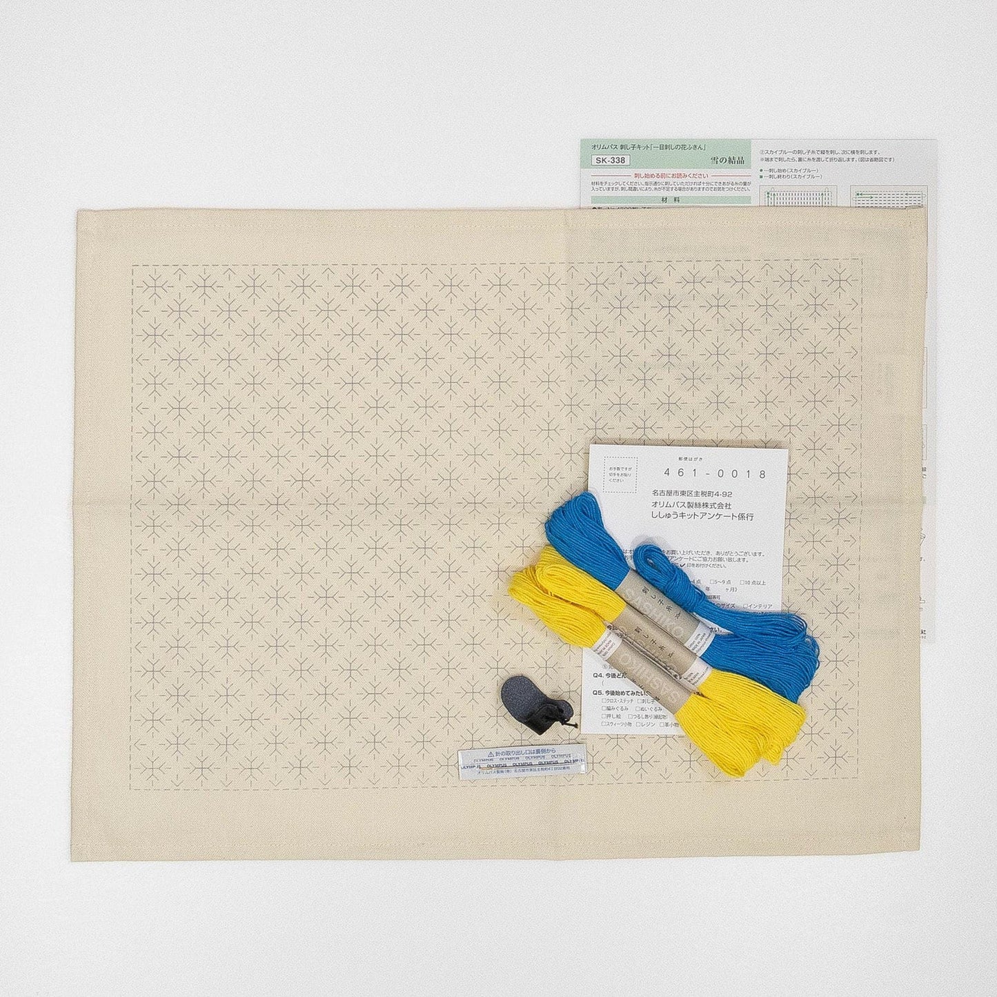 a beige fabric with a repeating star pattern, a pair of blue and yellow embroidery floss, and a small black object.