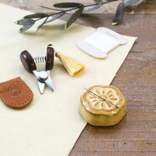 various sewing and crafting tools and materials, including a pair of scissors, a tassel, a spool of thread, and a small yellow object resembling a flower or ornament.