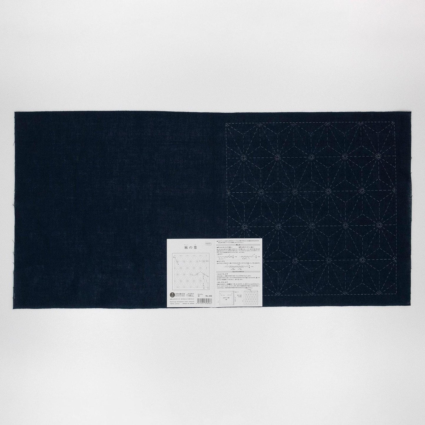 a dark blue fabric with a white pattern on it, and there is a small white label or instructions next to it.