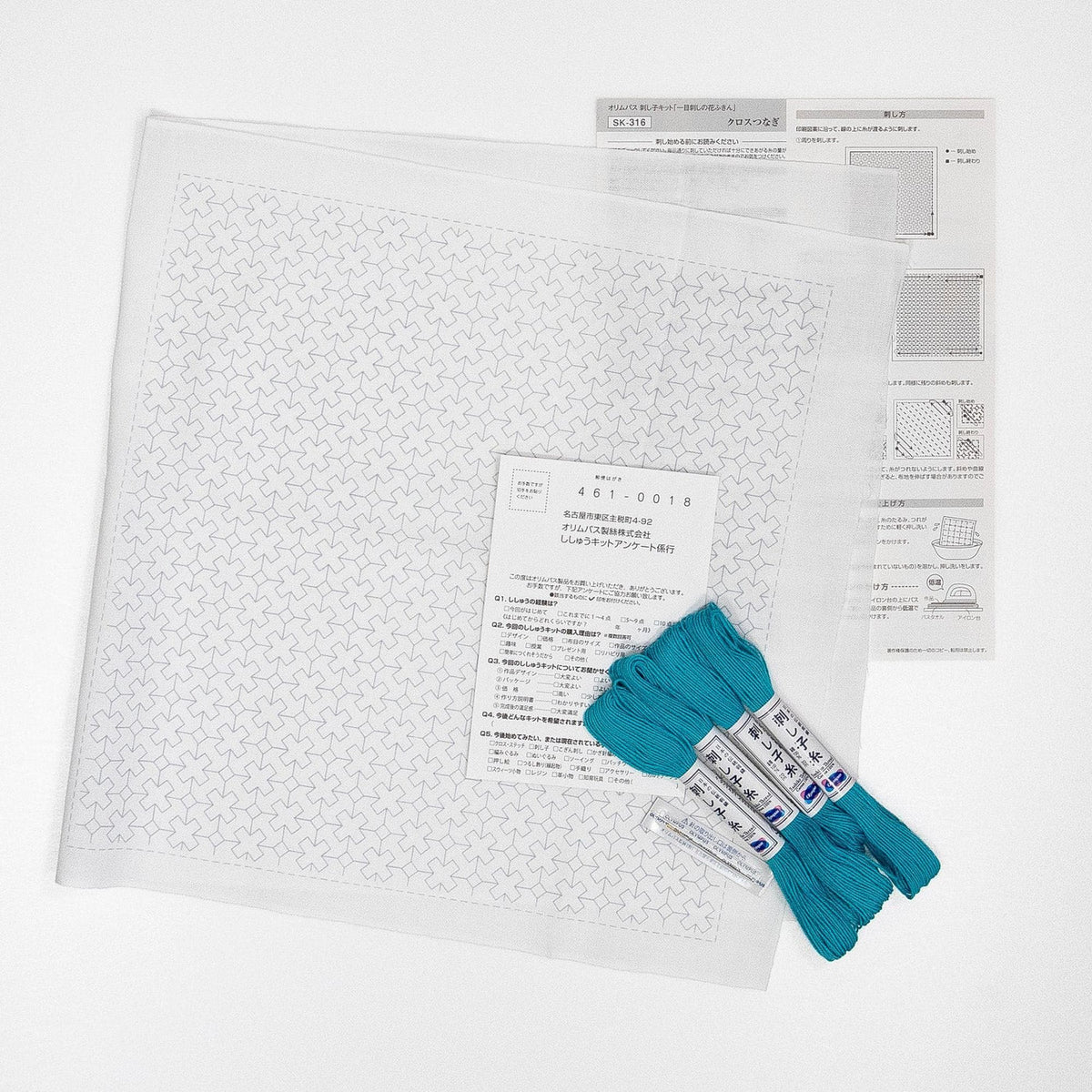 a square piece of paper with a pattern, a set of blue thread, and some instructions or information related to the pattern.