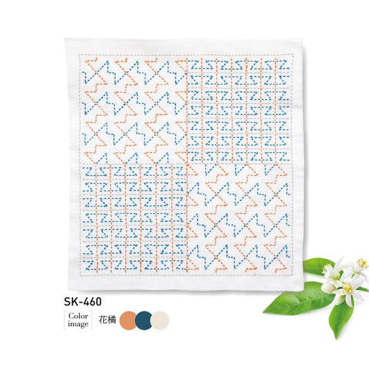 The image is a square piece of fabric with a repeating pattern of orange and blue geometric shapes, accompanied by a small white flower and green leaves.