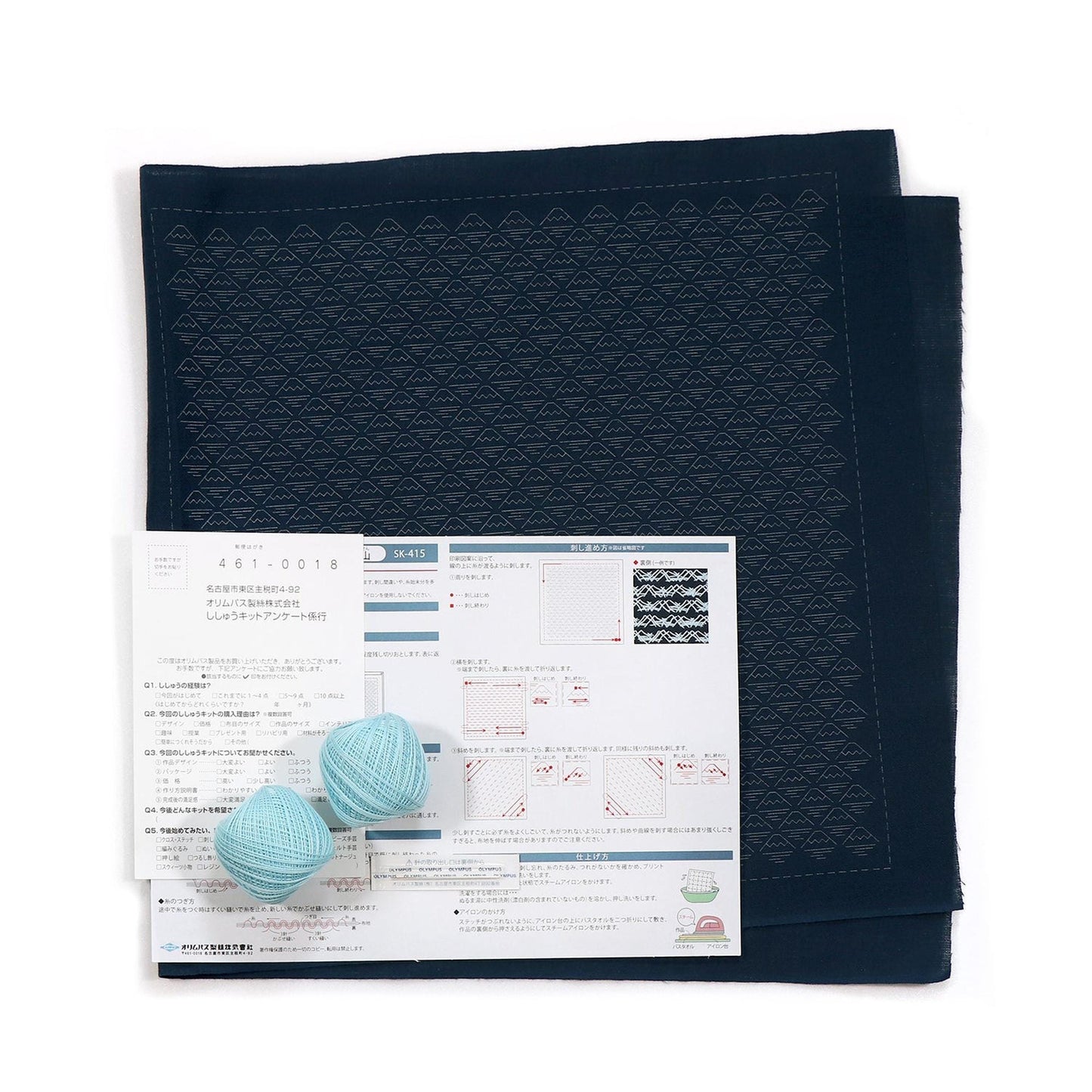 a black fabric with a geometric pattern, a white paper with Japanese text, and two blue balls of yarn.
