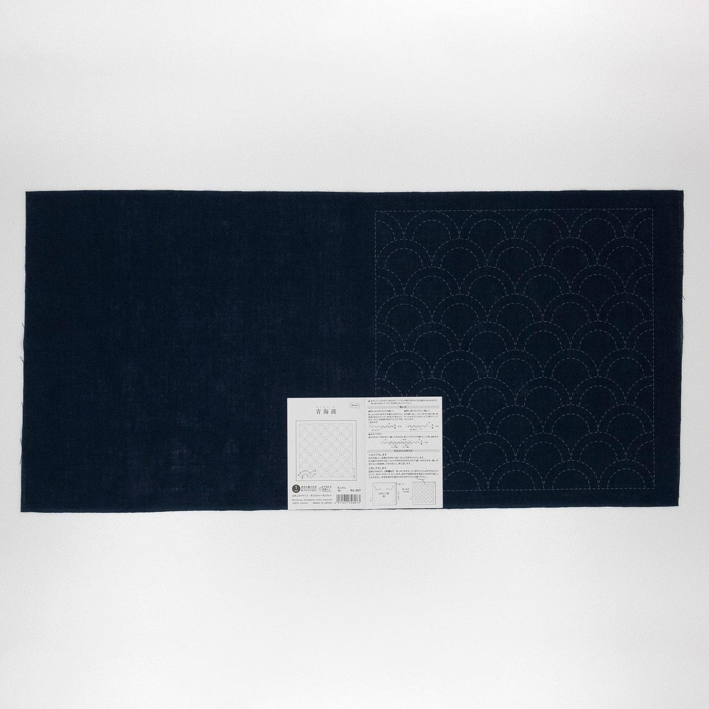 a dark blue fabric with a white pattern on it, placed on a white background. There is a small white label or instruction sheet attached to the fabric, but the text is not legible.