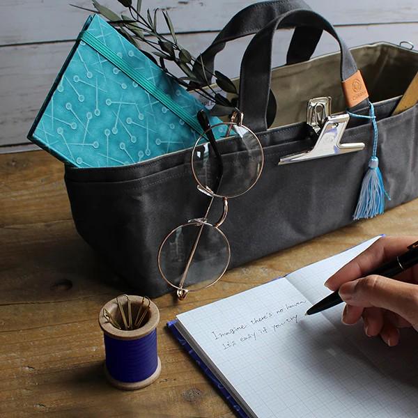 a person writing on a notebook with a bag in the background
