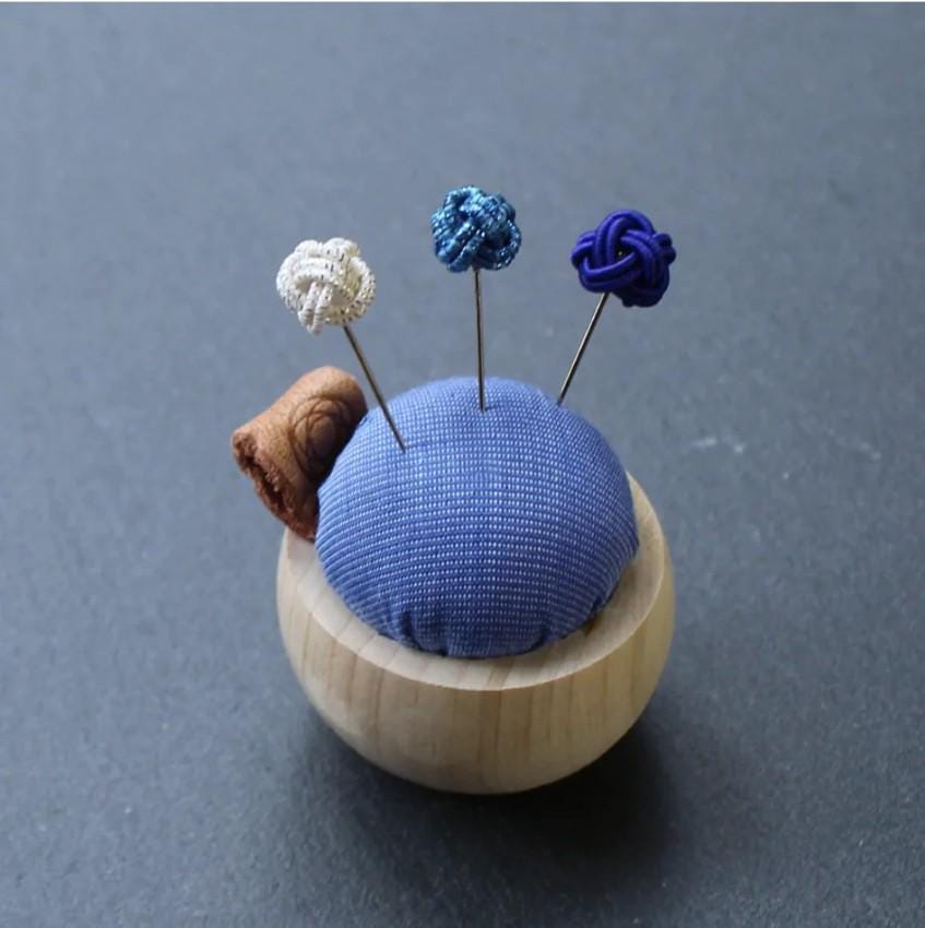 a blue pin cushion with three pins in it
