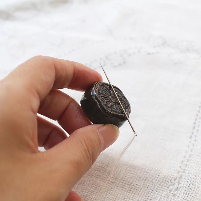 a person holding a needle and a button on a piece of cloth