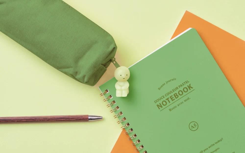 a green notebook with a pencil and a small toy