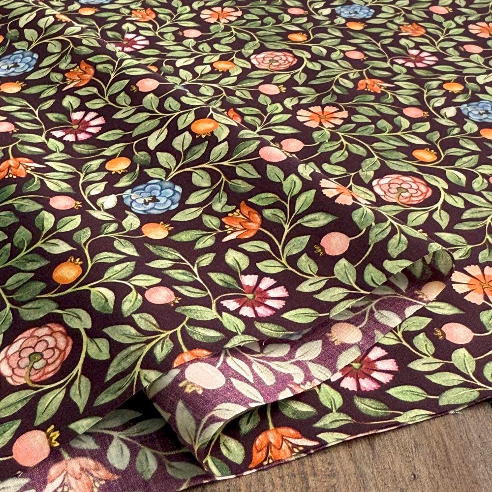 a close-up view of a fabric with a floral pattern. The fabric has a dark background with a repeating pattern of leaves, flowers, and fruits in various colors such as pink, orange, and blue.