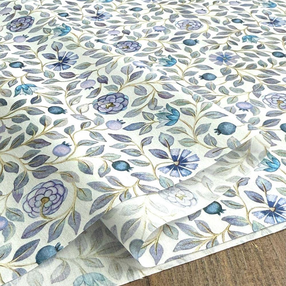 a close-up view of a fabric with a floral pattern, including various shades of blue and green flowers and leaves. The fabric appears to be a piece of paper or a textile, with the pattern repeated across its surface.