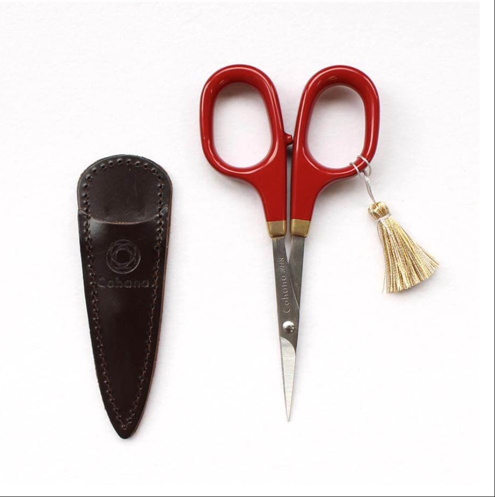 A pair of red scissors and a black leather pouch with a tassel are displayed against a white background.