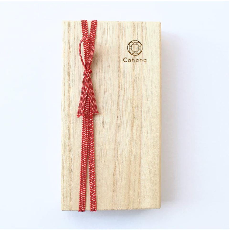A wooden box with a red ribbon tied around it, and the word "Cohana" printed on it.