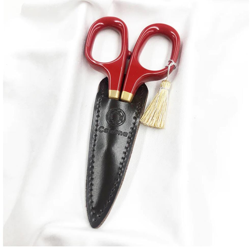 A pair of red-handled scissors with a black leather case and a gold tassel, placed on a white surface.