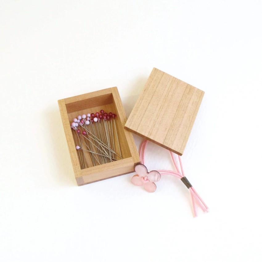 A wooden box containing a collection of colorful pins and a pink flower-shaped charm.