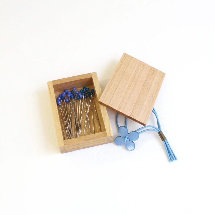 A wooden box containing blue pins and a blue tassel.